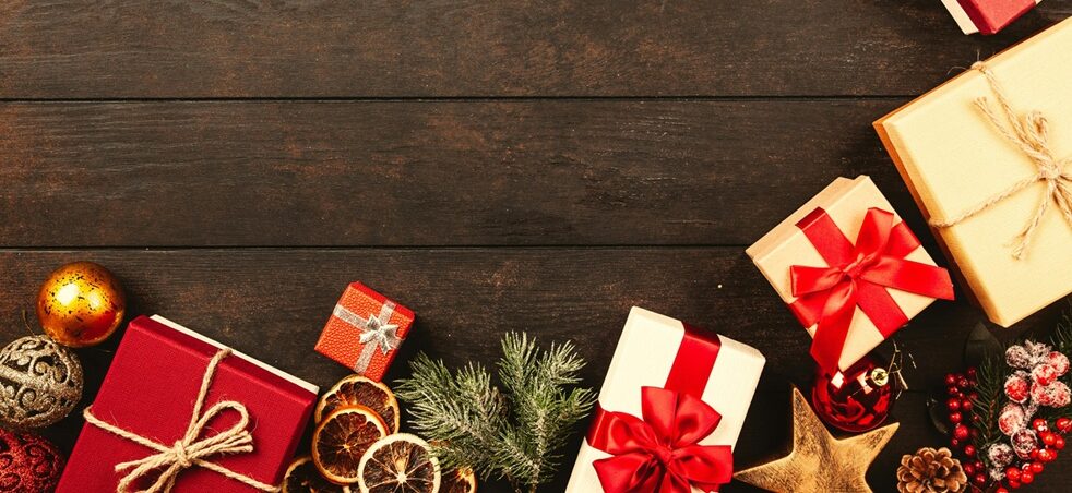 Wrapped Christmas presents with red ribbons, baubles, dried orange slices and pine sprigs on a dark wooden table