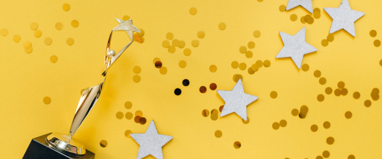 Gold star trophy surrounded by silver stars and gold confetti on a yellow background