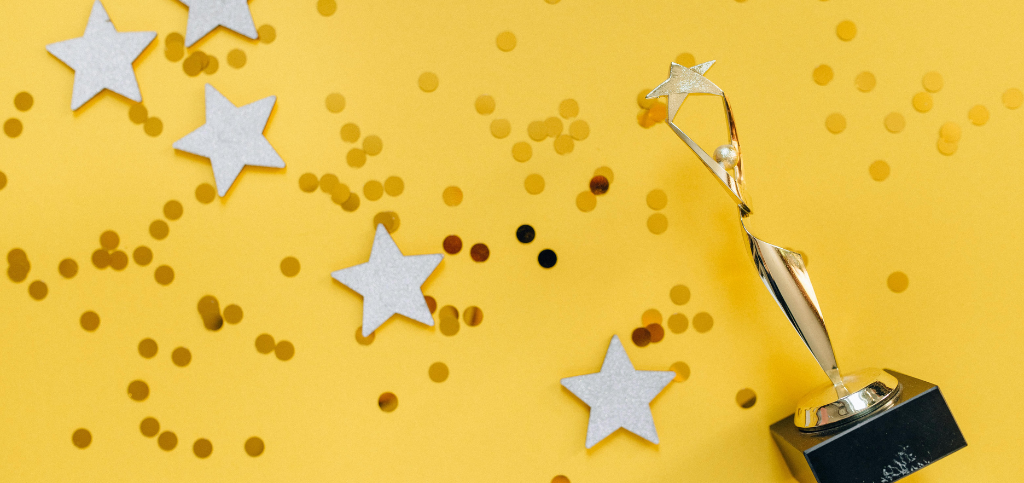 Gold star trophy on a yellow background scattered with silver stars and gold confetti